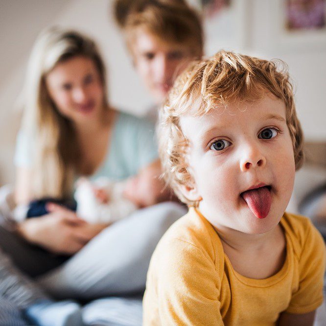 A small toddler boy with parents and newborn baby at home.